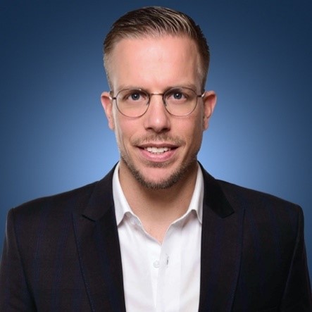 Person mit Brille und Anzug vor blauem Hintergrund.