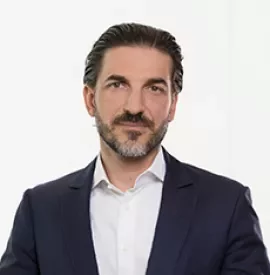 Person in Anzug mit weißem Hemd vor neutralem Hintergrund.