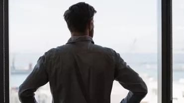 Person schaut aus einem Fenster auf einen Hafen.