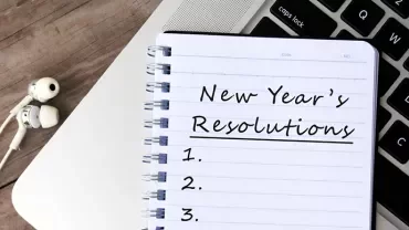 Notizbuch mit Neujahrsvorsätzen neben einem Laptop.