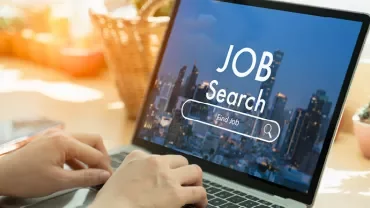 Person tippt auf einem Laptop mit 'Job Search' auf dem Bildschirm.