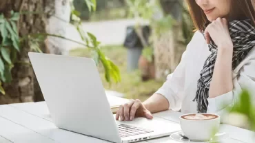Person arbeitet am Laptop im Freien neben einer Tasse Kaffee.