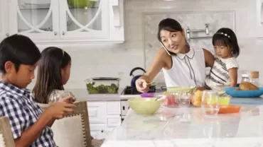 Familie in der Küche, Mutter telefoniert und serviert Snacks an der Theke.