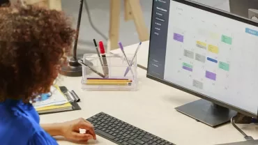 Person arbeitet am Schreibtisch mit Kalender auf Bildschirm