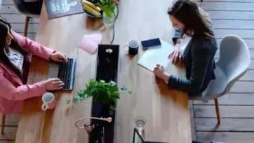 Zwei Personen arbeiten in einem Büro an einem Holztisch.