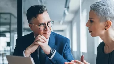 Zwei erwachsene Personen unterhalten sich in einem hellen Büro.