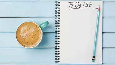 Notizbuch mit der Aufschrift 'To Do List' und einem Bleistift neben einer Tasse Kaffee auf blauem Tisch.