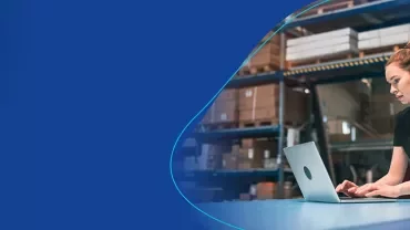 Frau sitzt am Computer in einer Lagerumgebung