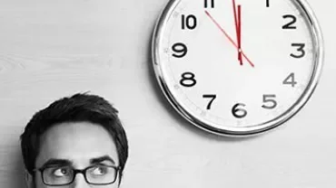 Person mit Brille schaut auf eine große Wanduhr.