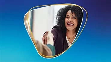 Eine Frau, die lächelt, während sie einer anderen Person vor blauem Hintergrund die Hand gibt.