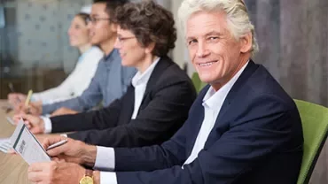 Personen bei einem Meeting, lächelnd und Notizen machend.