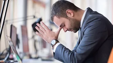 Person stützt den Kopf auf die Hände vor einem Laptop im Büro.