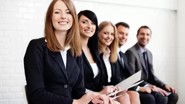 Gruppe von lächelnden Menschen in Businesskleidung, die auf einer Bank sitzen.