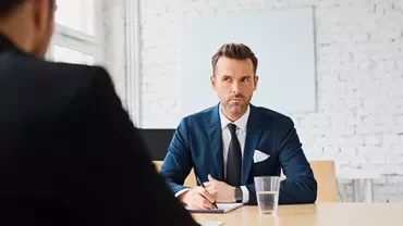 Person in Anzug sitzt an einem Tisch bei einem Meeting.