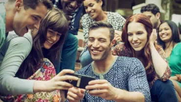 Gruppe von Freunden lächelt und schaut auf ein Handy.