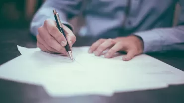 Person unterschreibt ein Dokument mit einem Kugelschreiber.