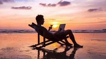 Person entspannt am Strand mit Laptop bei Sonnenuntergang.