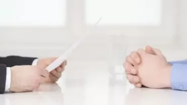 Zwei Personen sitzen am Tisch, die eine hält ein Papier.