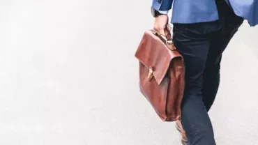 Person mit blauer Jacke trägt eine braune Ledertasche.