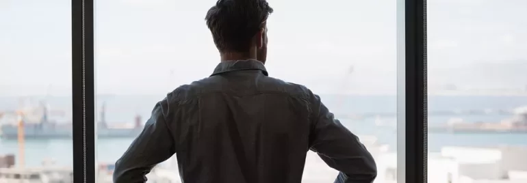 Person schaut aus einem Fenster auf einen Hafen.
