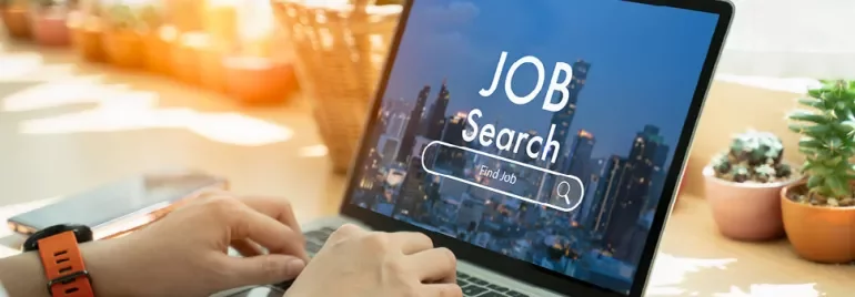 Person tippt auf einem Laptop mit 'Job Search' auf dem Bildschirm.