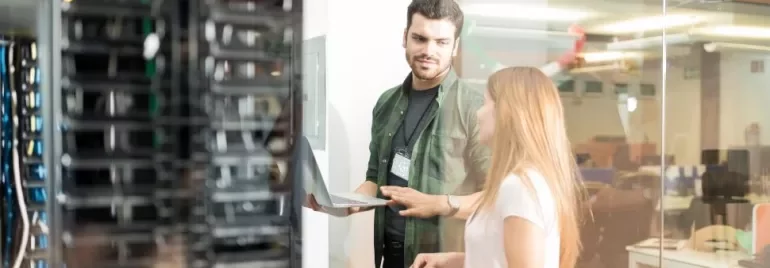 Zwei Personen in einem Serverraum, eine benutzt einen Laptop.