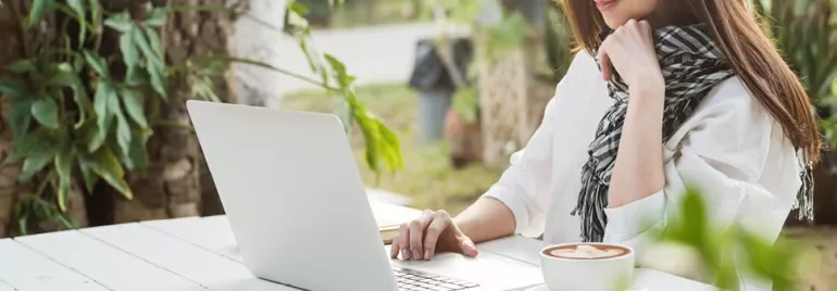 Person arbeitet am Laptop im Freien neben einer Tasse Kaffee.