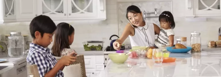Familie in der Küche, Mutter telefoniert und serviert Snacks an der Theke.