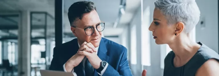 Zwei erwachsene Personen unterhalten sich in einem hellen Büro.