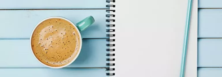 Notizbuch mit der Aufschrift 'To Do List' und einem Bleistift neben einer Tasse Kaffee auf blauem Tisch.