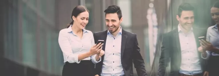 Zwei Personen gehen und lachen, während sie auf ein Handy schauen.