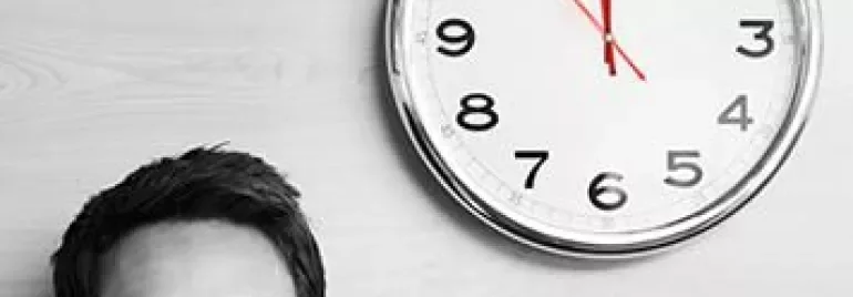 Person mit Brille schaut auf eine große Wanduhr.