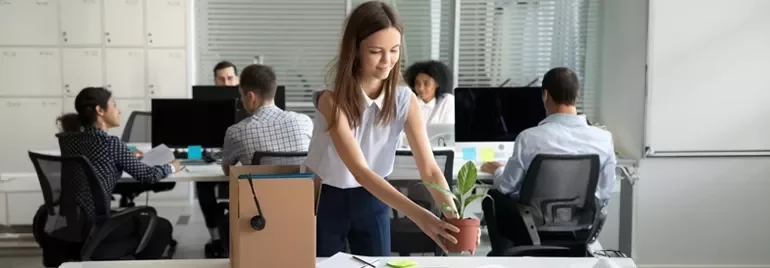 Person richtet einen Arbeitsplatz mit einer Pflanze und einem Karton im Büro ein.