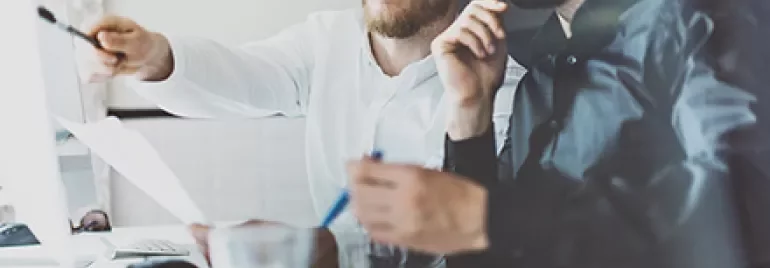 Zwei Personen arbeiten am Computer, eine zeigt auf den Bildschirm.
