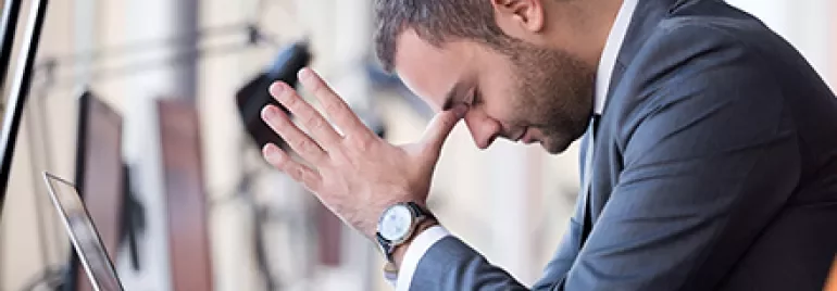 Person stützt den Kopf auf die Hände vor einem Laptop im Büro.