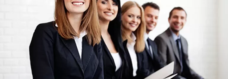 Gruppe von lächelnden Menschen in Businesskleidung, die auf einer Bank sitzen.