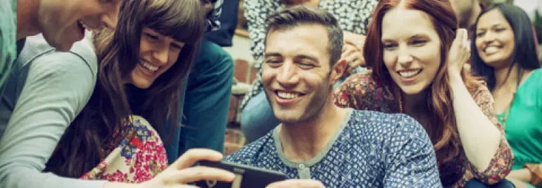 Gruppe von Freunden lächelt und schaut auf ein Handy.