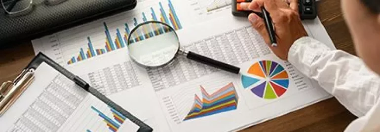 Person analysiert Diagramme und Berechnungen mit Taschenrechner.