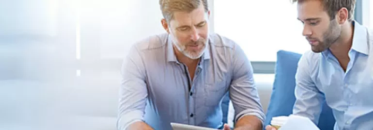 Zwei Personen diskutieren in einem Büro mit einem Tablet und Dokumenten.
