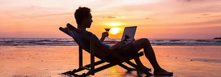 Person entspannt am Strand mit Laptop bei Sonnenuntergang.
