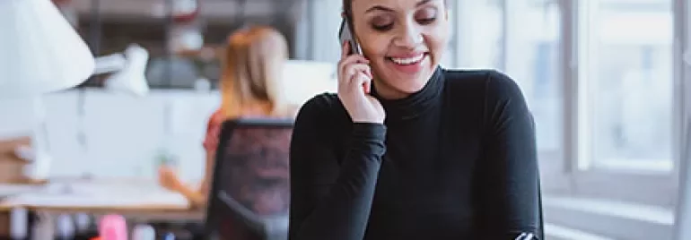 Person telefoniert und notiert etwas im Büro.