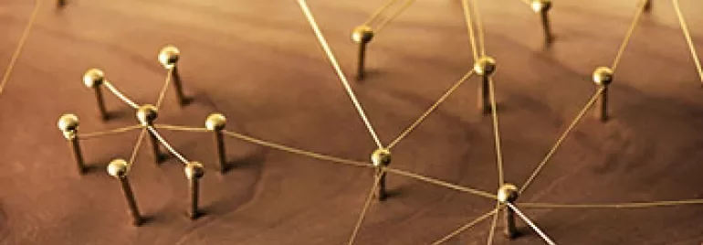 Holzbrett mit goldenen Fäden und Nägeln, die ein Netzwerk bilden.