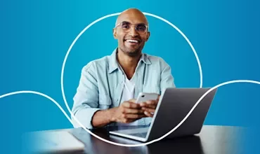 Person sitzt an einem Laptop, lächelt, vor blauem Hintergrund.
