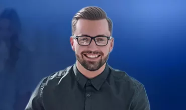 Ein fröhlicher Mann mit Brille und Bart, der herzlich lächelt.