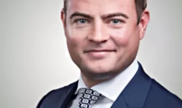Eine Person in einem blauen Anzug mit weißem Hemd und gemusterter Krawatte.