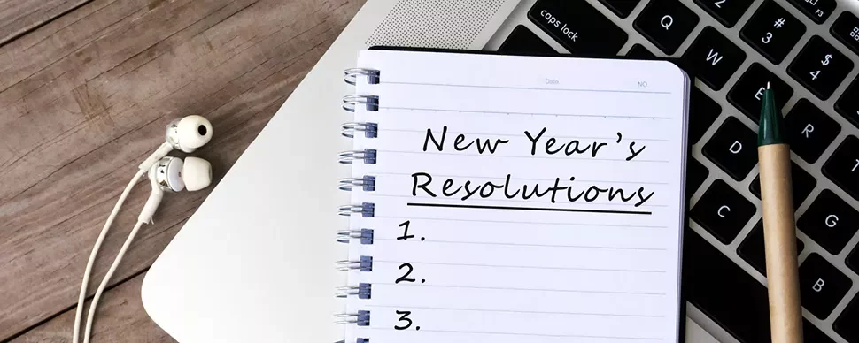 Notizbuch mit Neujahrsvorsätzen neben einem Laptop.