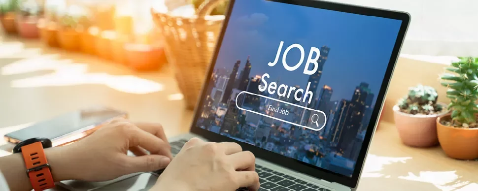 Person tippt auf einem Laptop mit 'Job Search' auf dem Bildschirm.