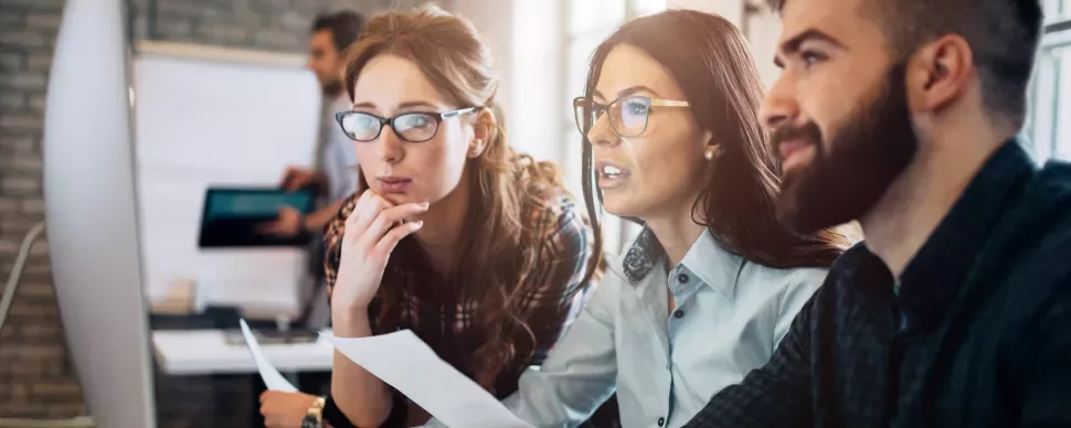 Drei Personen arbeiten am Computer und besprechen ein Projekt.