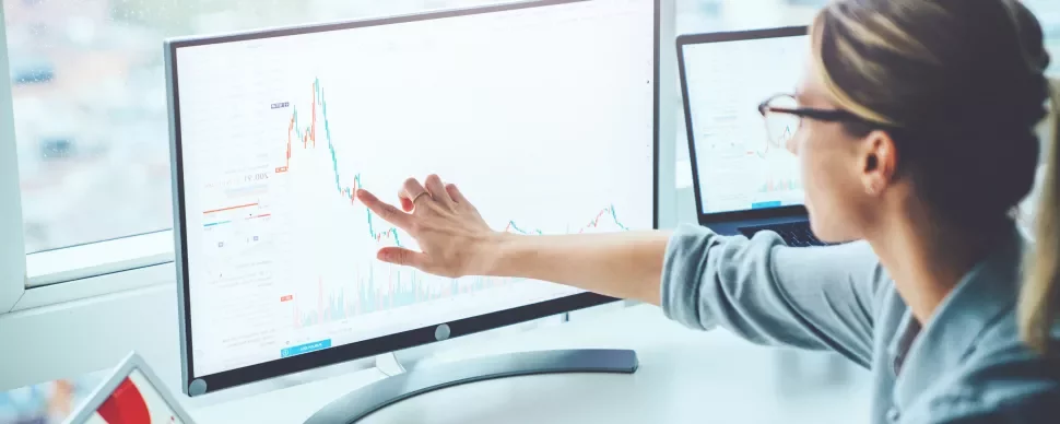 Person zeigt auf einen Bildschirm mit Finanzdiagramm.