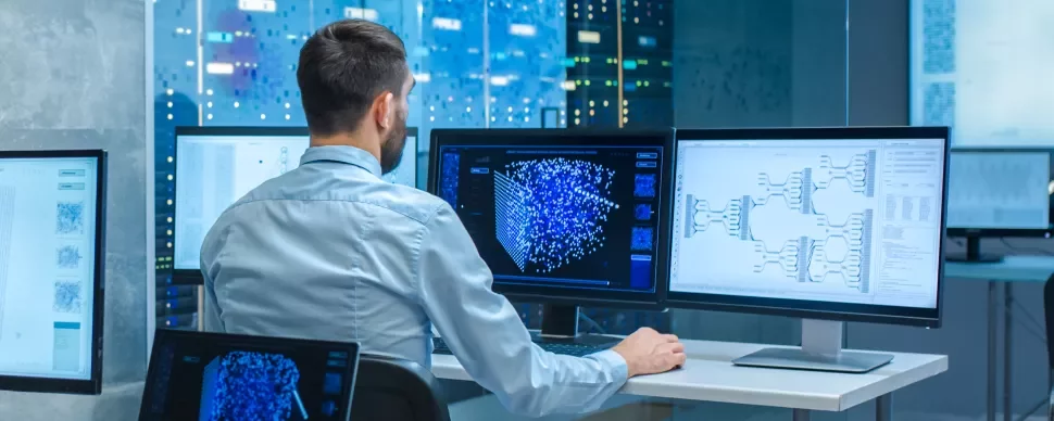 Person arbeitet am Computer mit mehreren Bildschirmen in einem modernen Büro.